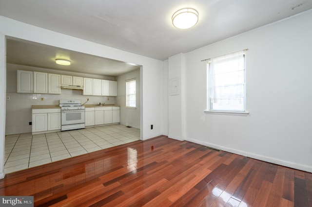 kitchen featuring backsplash, white range oven, sink, light hardwood / wood-style flooring, and white cabinetry