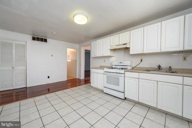 kitchen featuring decorative backsplash, white gas stove, white cabinets, and sink