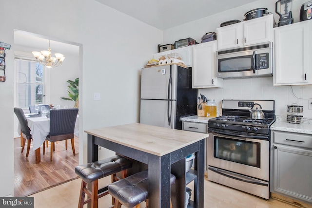 kitchen featuring white cabinetry, hanging light fixtures, stainless steel appliances, a chandelier, and decorative backsplash