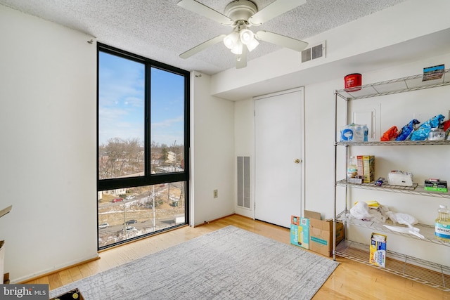 interior space featuring ceiling fan, wood-type flooring, a textured ceiling, and a wall of windows