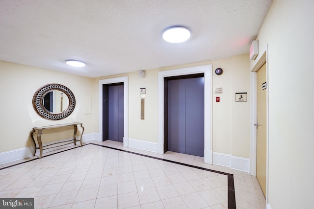 interior space with a textured ceiling, elevator, and light tile patterned flooring