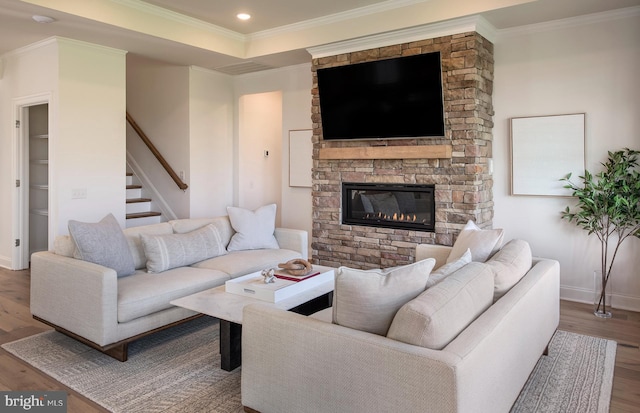 living room with a raised ceiling, hardwood / wood-style flooring, a stone fireplace, and crown molding