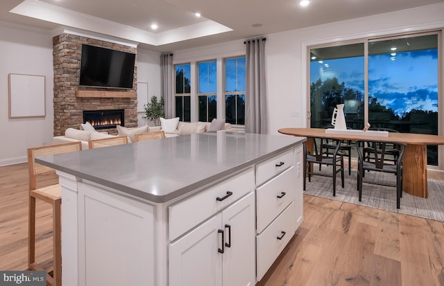 kitchen with white cabinets, a stone fireplace, light wood-type flooring, a tray ceiling, and a kitchen island