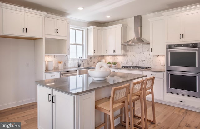 kitchen featuring white cabinetry, a center island, wall chimney range hood, and appliances with stainless steel finishes