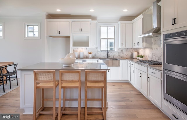 kitchen featuring white cabinetry, a center island, wall chimney exhaust hood, a kitchen bar, and appliances with stainless steel finishes