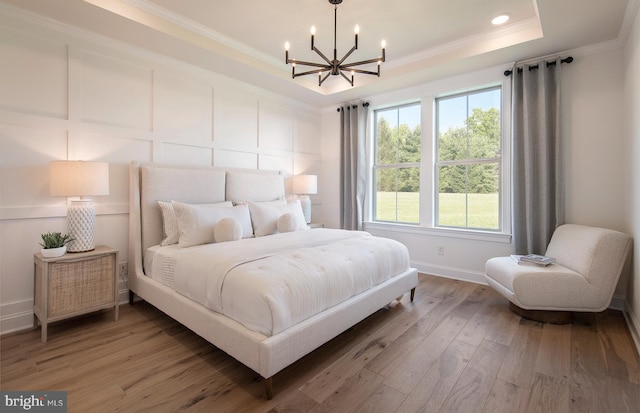 bedroom with hardwood / wood-style floors, a tray ceiling, crown molding, and a notable chandelier