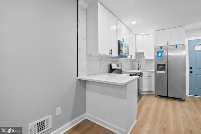 kitchen with appliances with stainless steel finishes, backsplash, light wood-type flooring, sink, and white cabinets