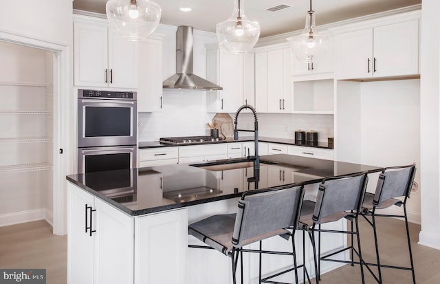 kitchen with a center island with sink, white cabinetry, stainless steel appliances, and wall chimney exhaust hood