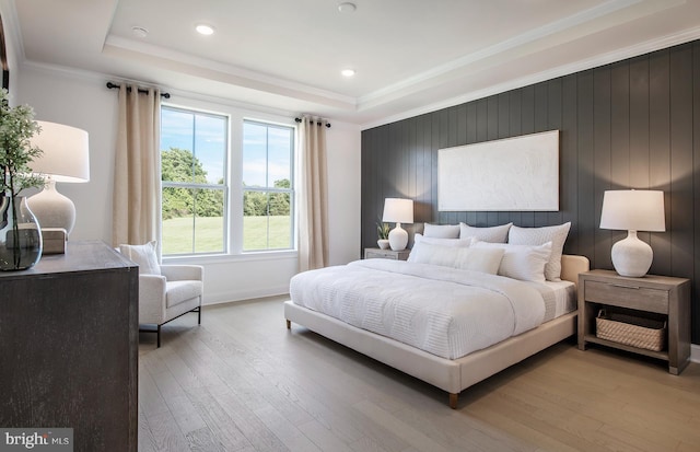 bedroom with light wood-type flooring, a tray ceiling, and ornamental molding