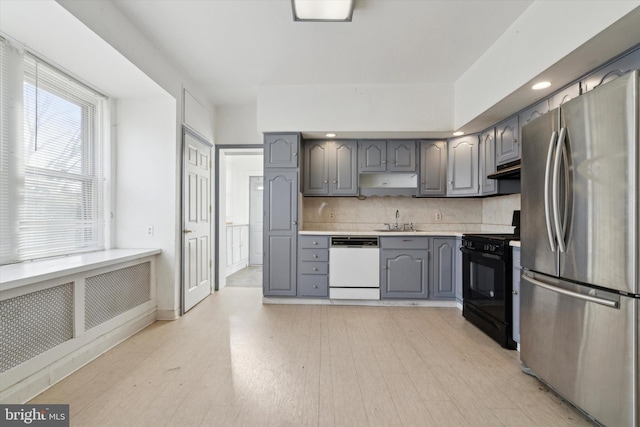 kitchen featuring dishwasher, stainless steel fridge, black range oven, and gray cabinetry