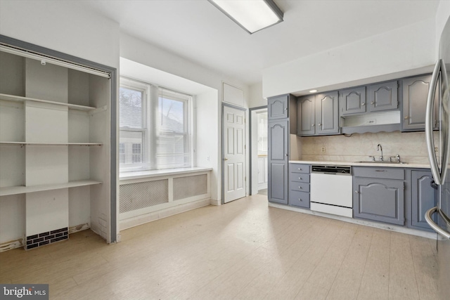 kitchen with dishwasher, backsplash, sink, gray cabinets, and light wood-type flooring