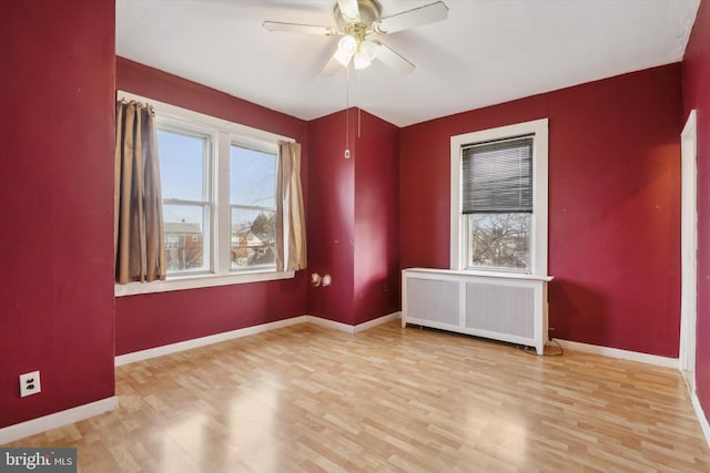 unfurnished room featuring ceiling fan, plenty of natural light, radiator, and light hardwood / wood-style flooring