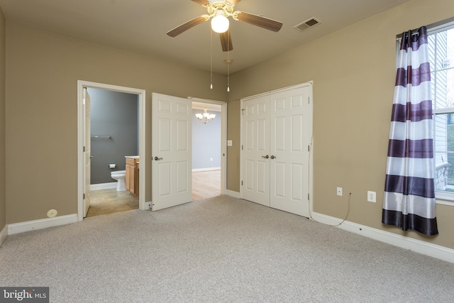 unfurnished bedroom featuring ceiling fan with notable chandelier, light colored carpet, ensuite bathroom, and a closet