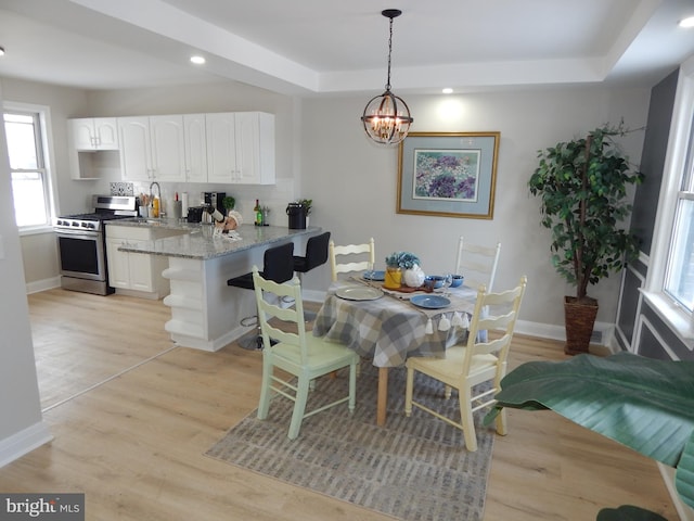 dining area featuring a tray ceiling, sink, a notable chandelier, and light wood-type flooring