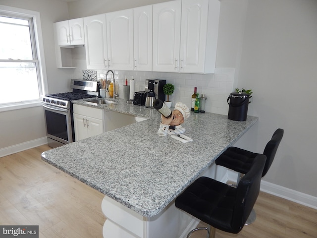 kitchen featuring white cabinetry, stainless steel gas stove, sink, light stone counters, and kitchen peninsula