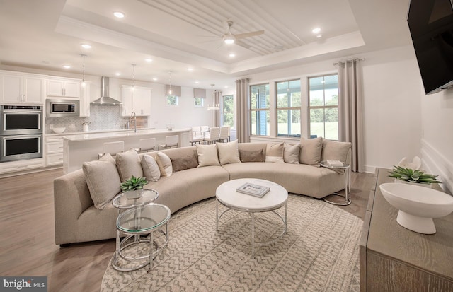 living room with ceiling fan, a raised ceiling, crown molding, and light hardwood / wood-style flooring