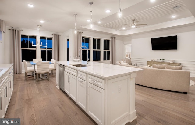 kitchen with white cabinetry, ceiling fan, an island with sink, pendant lighting, and a tray ceiling