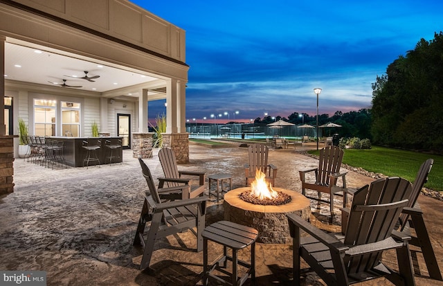 patio terrace at dusk with exterior bar, an outdoor fire pit, and ceiling fan