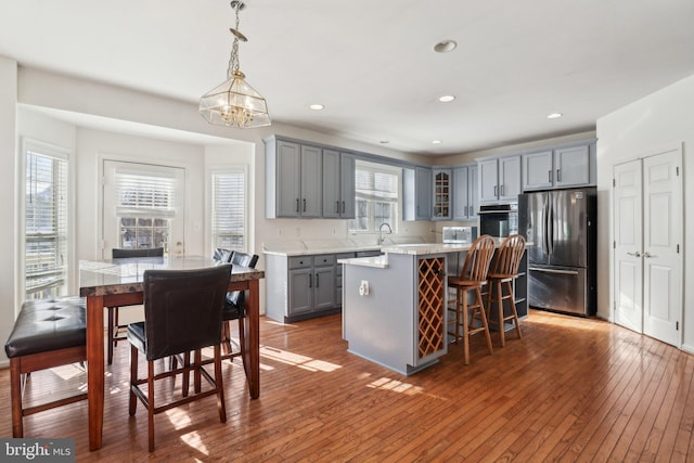 kitchen featuring stainless steel refrigerator, decorative light fixtures, gray cabinets, a kitchen island, and hardwood / wood-style flooring