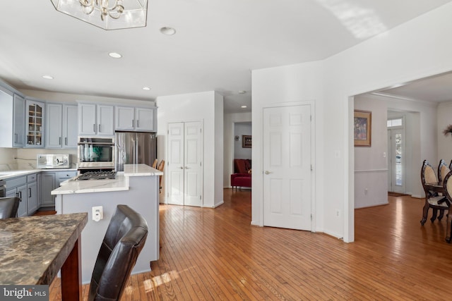 kitchen featuring gray cabinetry, stainless steel appliances, light hardwood / wood-style floors, decorative light fixtures, and a kitchen island