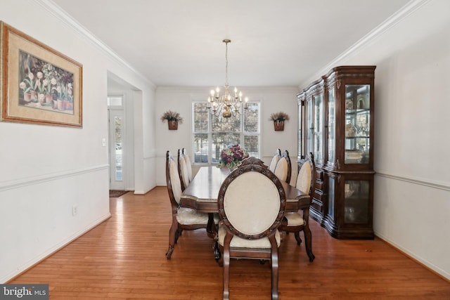 dining space with hardwood / wood-style floors, ornamental molding, and a notable chandelier