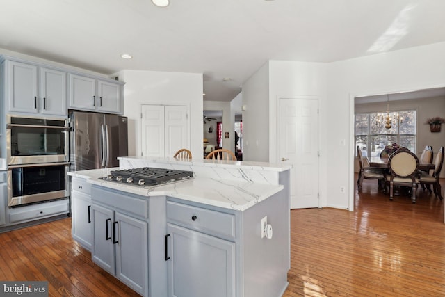 kitchen with an inviting chandelier, hanging light fixtures, dark hardwood / wood-style floors, appliances with stainless steel finishes, and a kitchen island