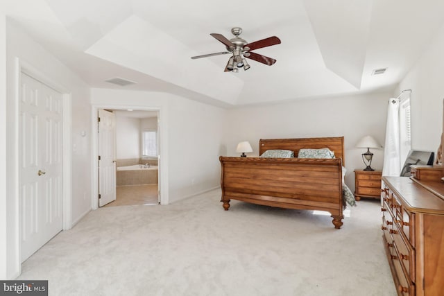 bedroom with ceiling fan, light carpet, connected bathroom, and a tray ceiling