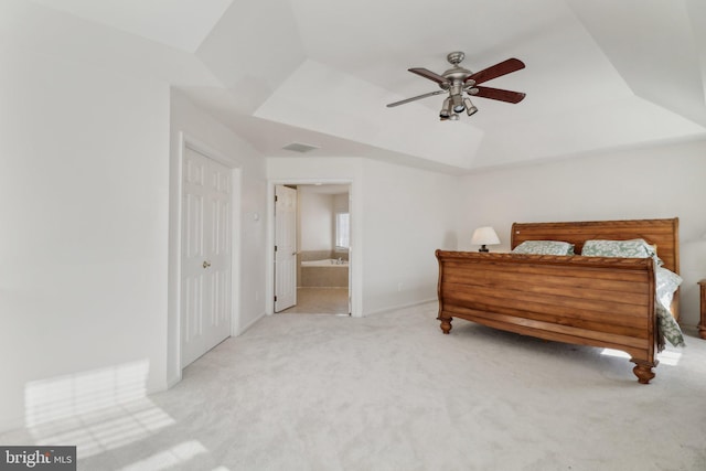 carpeted bedroom featuring ceiling fan, a raised ceiling, and ensuite bath