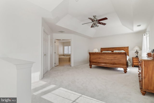 bedroom with a tray ceiling, connected bathroom, ceiling fan, and light carpet