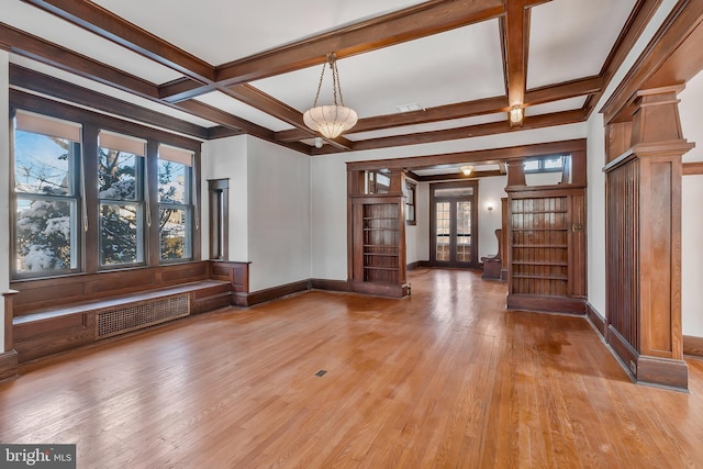 unfurnished living room with beamed ceiling, a healthy amount of sunlight, a chandelier, and french doors