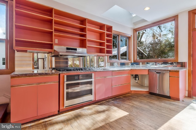 kitchen with extractor fan, a skylight, light hardwood / wood-style flooring, stone counters, and stainless steel appliances