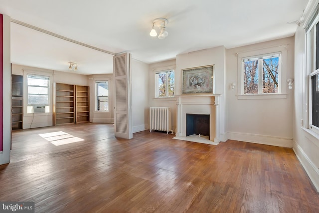 unfurnished living room featuring radiator, wood-type flooring, and a healthy amount of sunlight