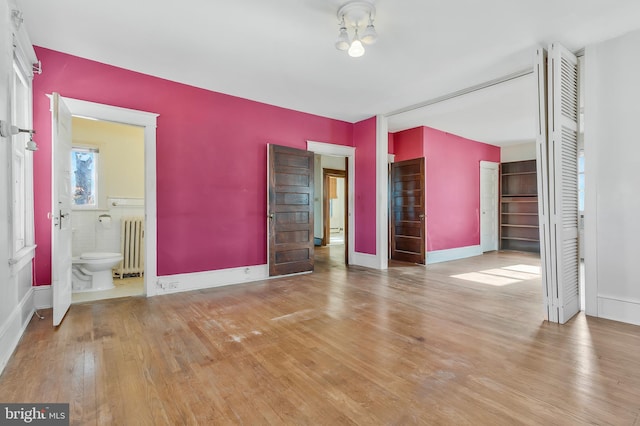 unfurnished bedroom with radiator heating unit, ensuite bathroom, and light wood-type flooring