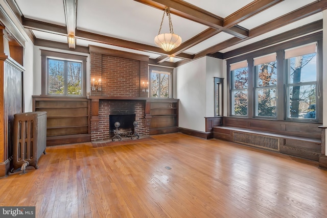 unfurnished living room featuring coffered ceiling, radiator, beamed ceiling, a fireplace, and light hardwood / wood-style floors