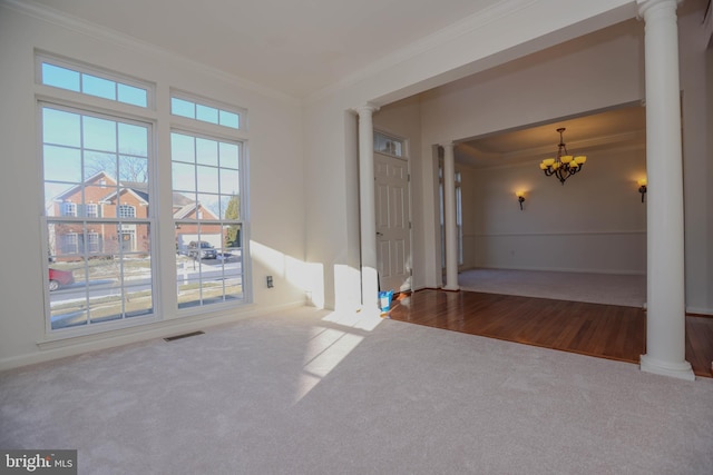 carpeted empty room with a notable chandelier, ornamental molding, and ornate columns