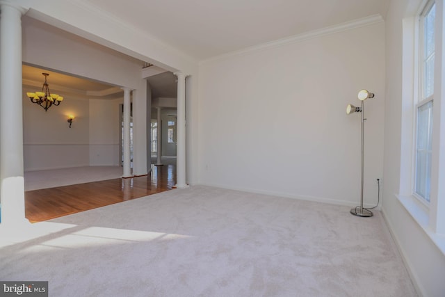 carpeted spare room with a notable chandelier, ornamental molding, and ornate columns