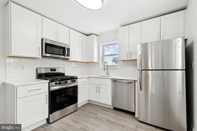 kitchen with white cabinetry, sink, stainless steel appliances, backsplash, and light wood-type flooring