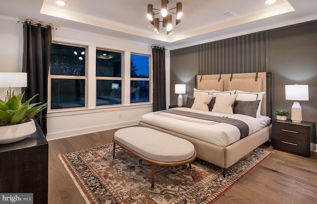 bedroom featuring an inviting chandelier, hardwood / wood-style flooring, a raised ceiling, and crown molding