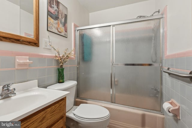 full bathroom featuring vanity, toilet, combined bath / shower with glass door, and tile walls