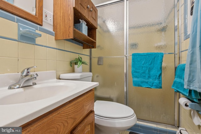 bathroom featuring vanity, a shower with door, toilet, tile walls, and tasteful backsplash