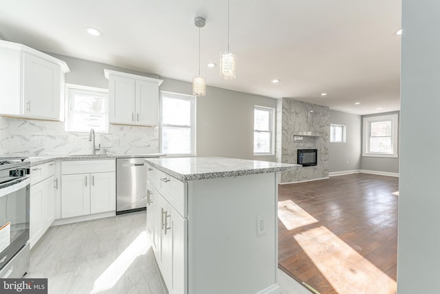 kitchen featuring a kitchen island, stainless steel dishwasher, decorative backsplash, a fireplace, and white cabinets