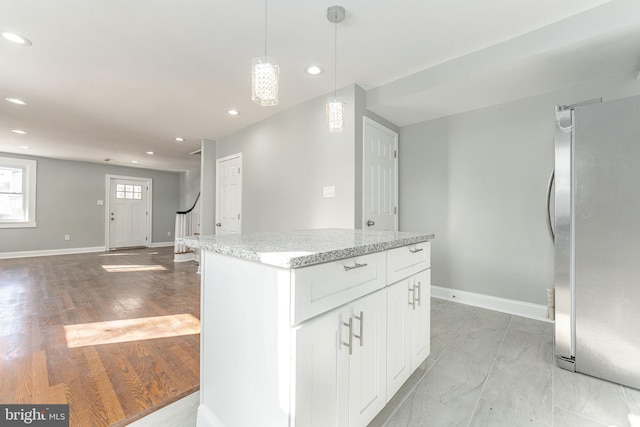 kitchen with stainless steel refrigerator, white cabinetry, a center island, light stone counters, and decorative light fixtures