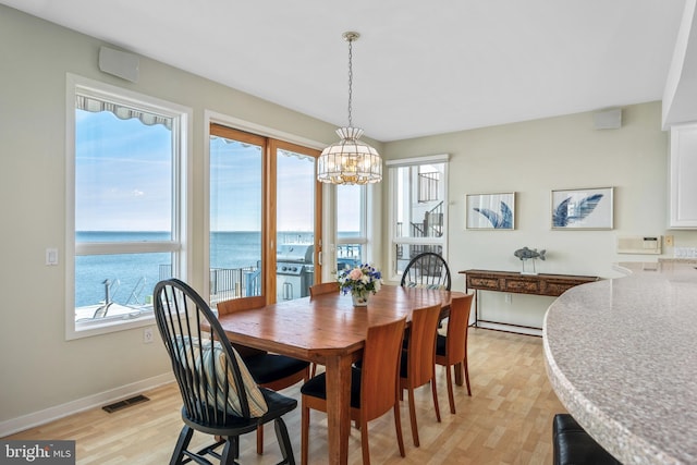 dining area with baseboard heating, a water view, light hardwood / wood-style flooring, and a notable chandelier