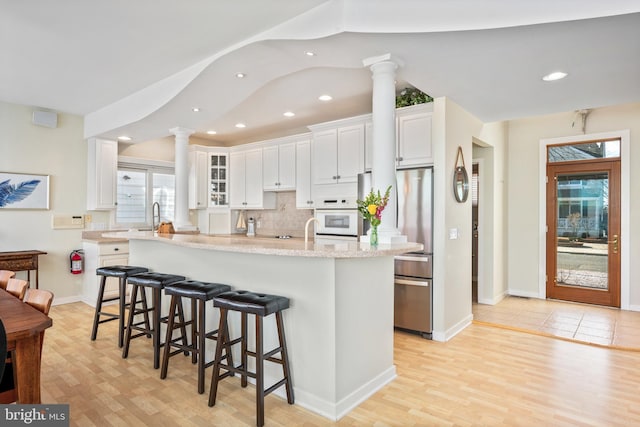 kitchen with stainless steel fridge, an island with sink, a breakfast bar area, light wood-type flooring, and white cabinets