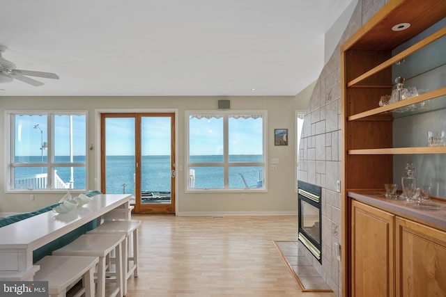 kitchen featuring ceiling fan, a tile fireplace, light hardwood / wood-style floors, a breakfast bar, and a water view