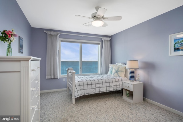 bedroom featuring ceiling fan, a water view, light colored carpet, and multiple windows