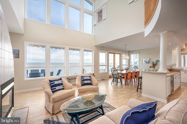 living room featuring a water view, light hardwood / wood-style floors, a towering ceiling, and decorative columns