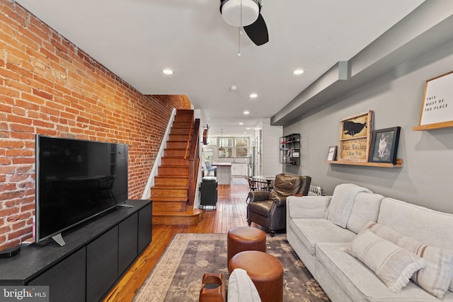 living room with hardwood / wood-style floors, ceiling fan, and brick wall