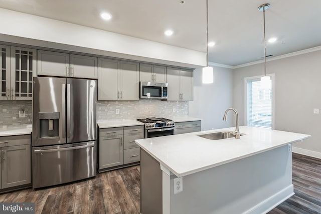 kitchen with gray cabinetry, stainless steel appliances, sink, hanging light fixtures, and a center island with sink