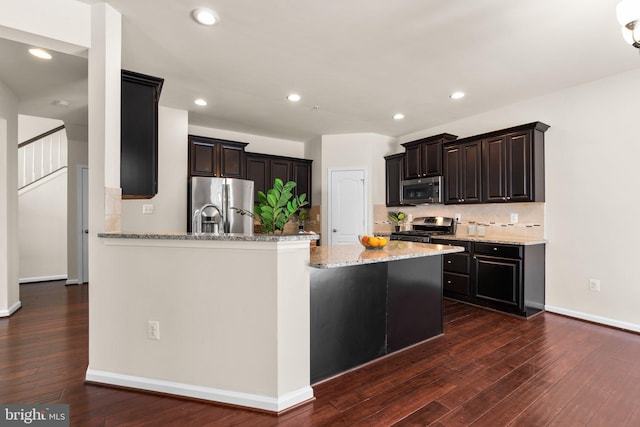 kitchen with dark wood-type flooring, appliances with stainless steel finishes, a kitchen island, and tasteful backsplash